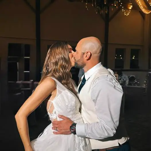 Bride and groom sharing a kiss during their wedding reception, embracing each other in a dimly lit venue.